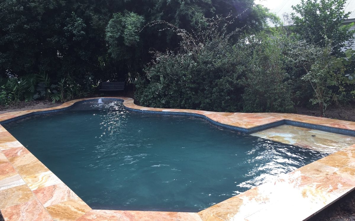 Free-form pool with dark water and a warm stone deck